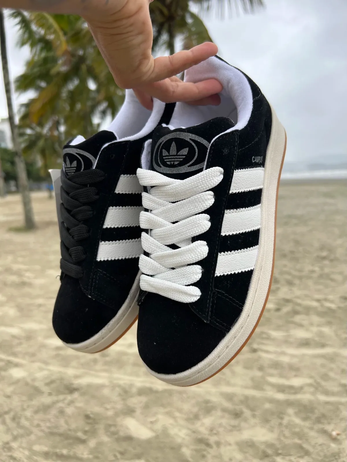 Adidas Campus 00s preto na mão, com a praia ao fundo