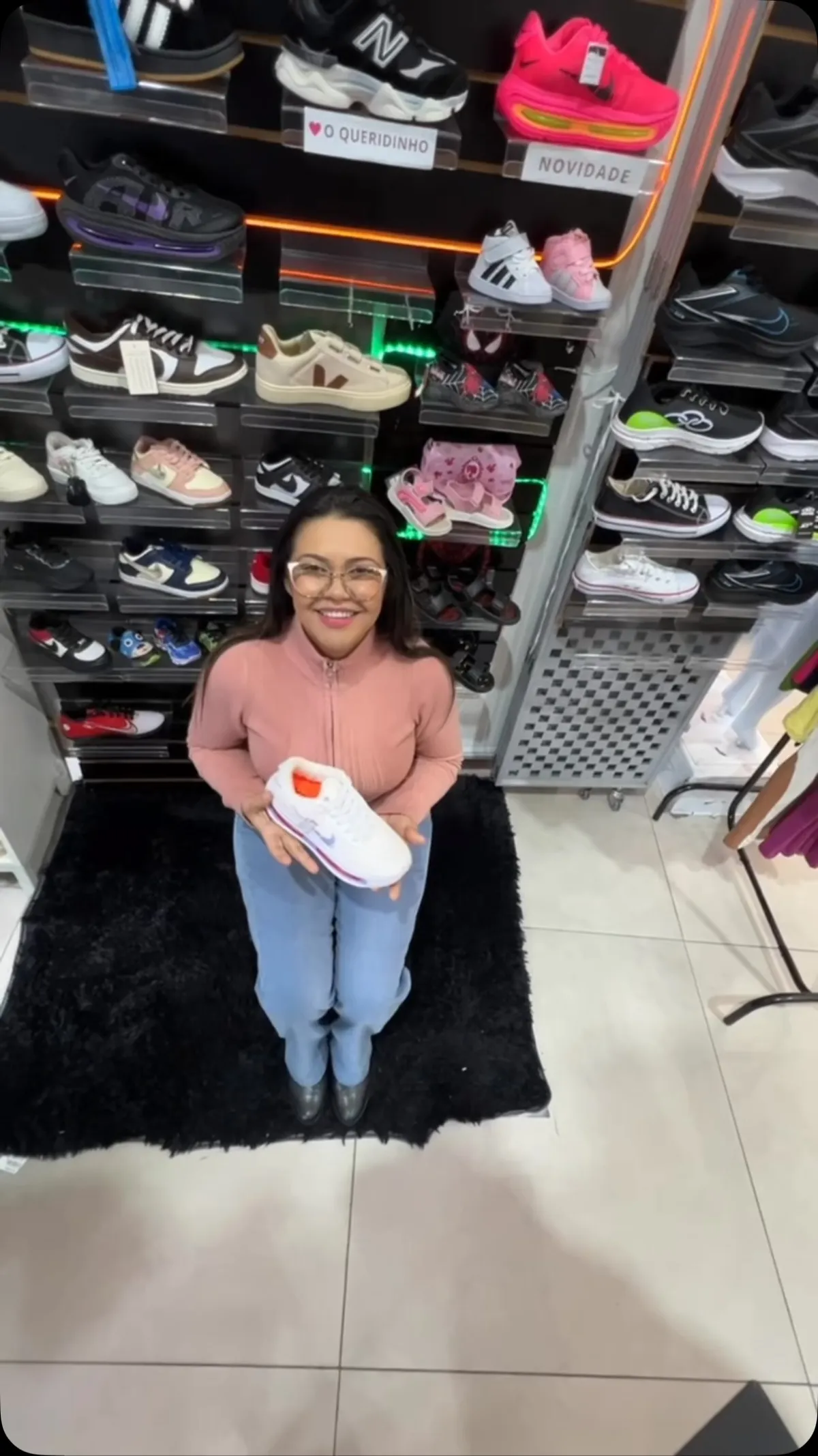 Vendedora da AL Multimarcas na loja, segurando um tênis, com a parede de tênis atrás